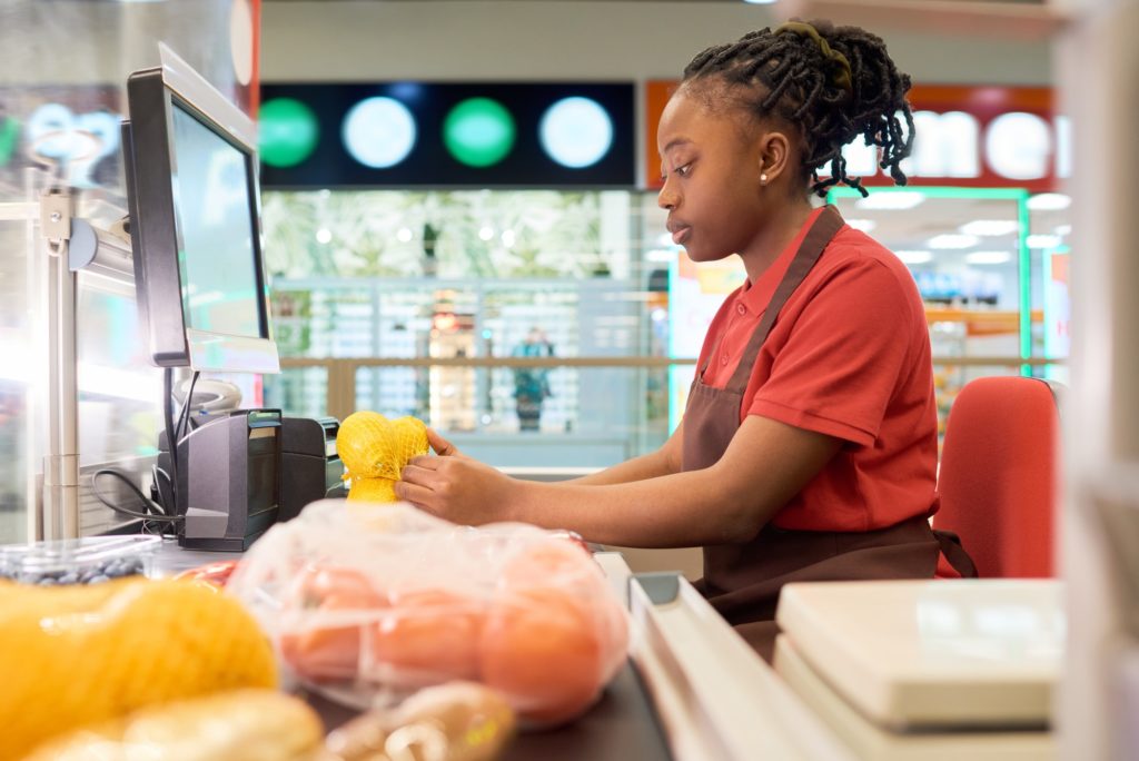Young female shop assistant scanning fresh lemons in bag by counter
