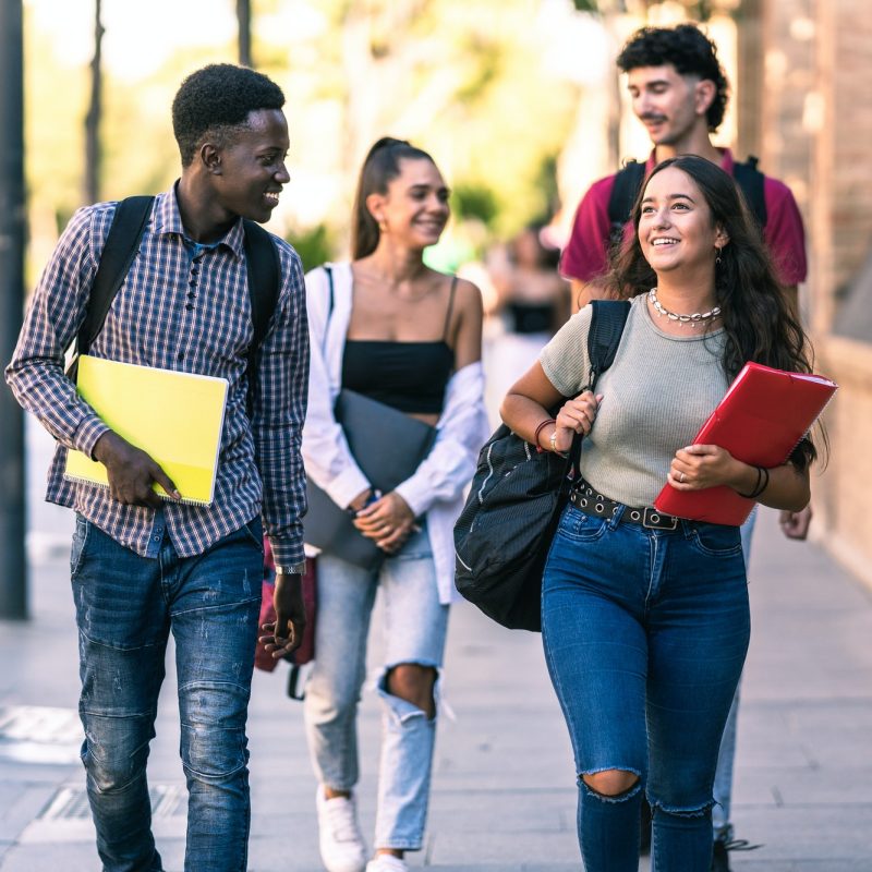 Four students of different ethnicities walking in outdoors with school material